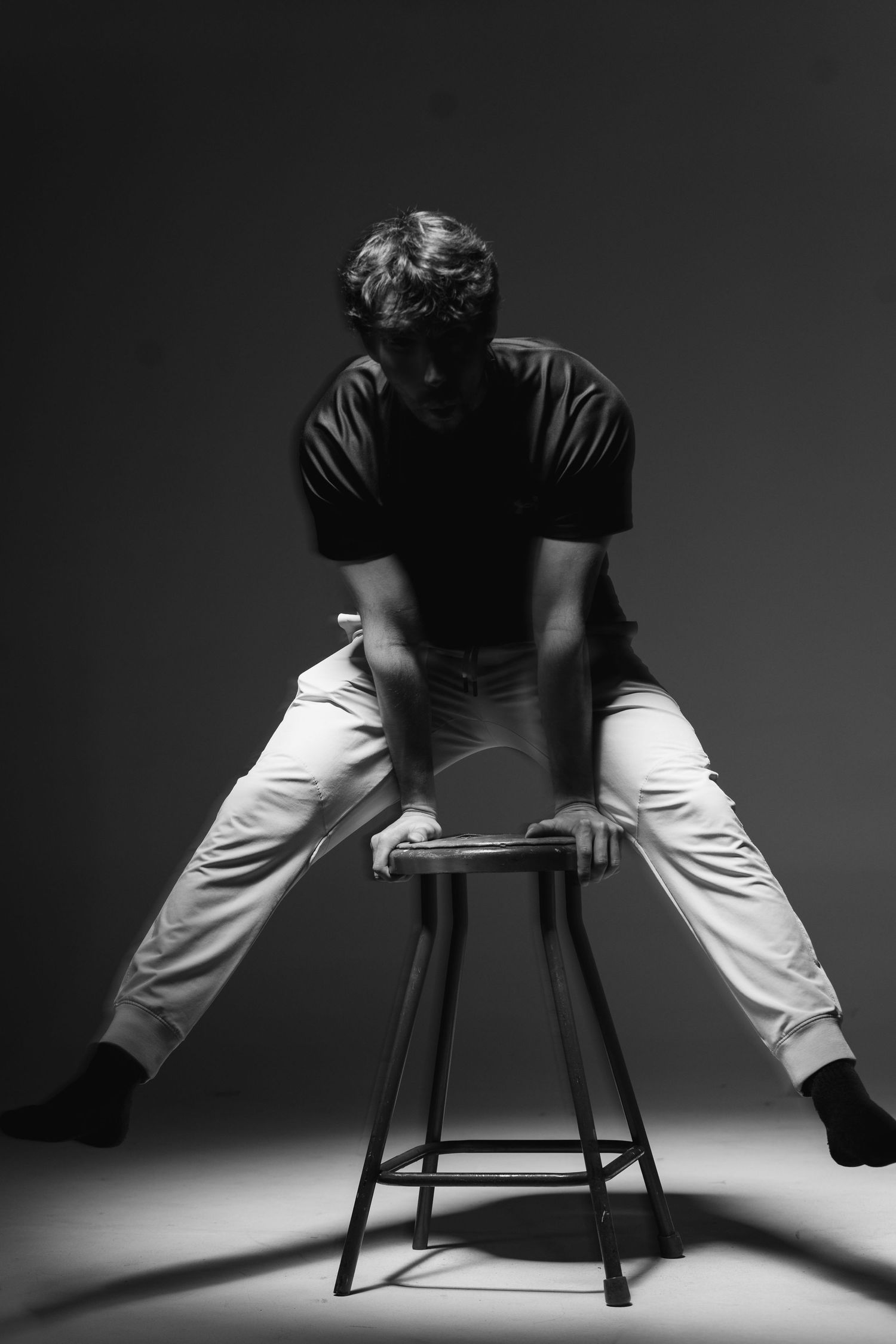 Flash studio portrait of a young white man balancing on a stool with just his hands.