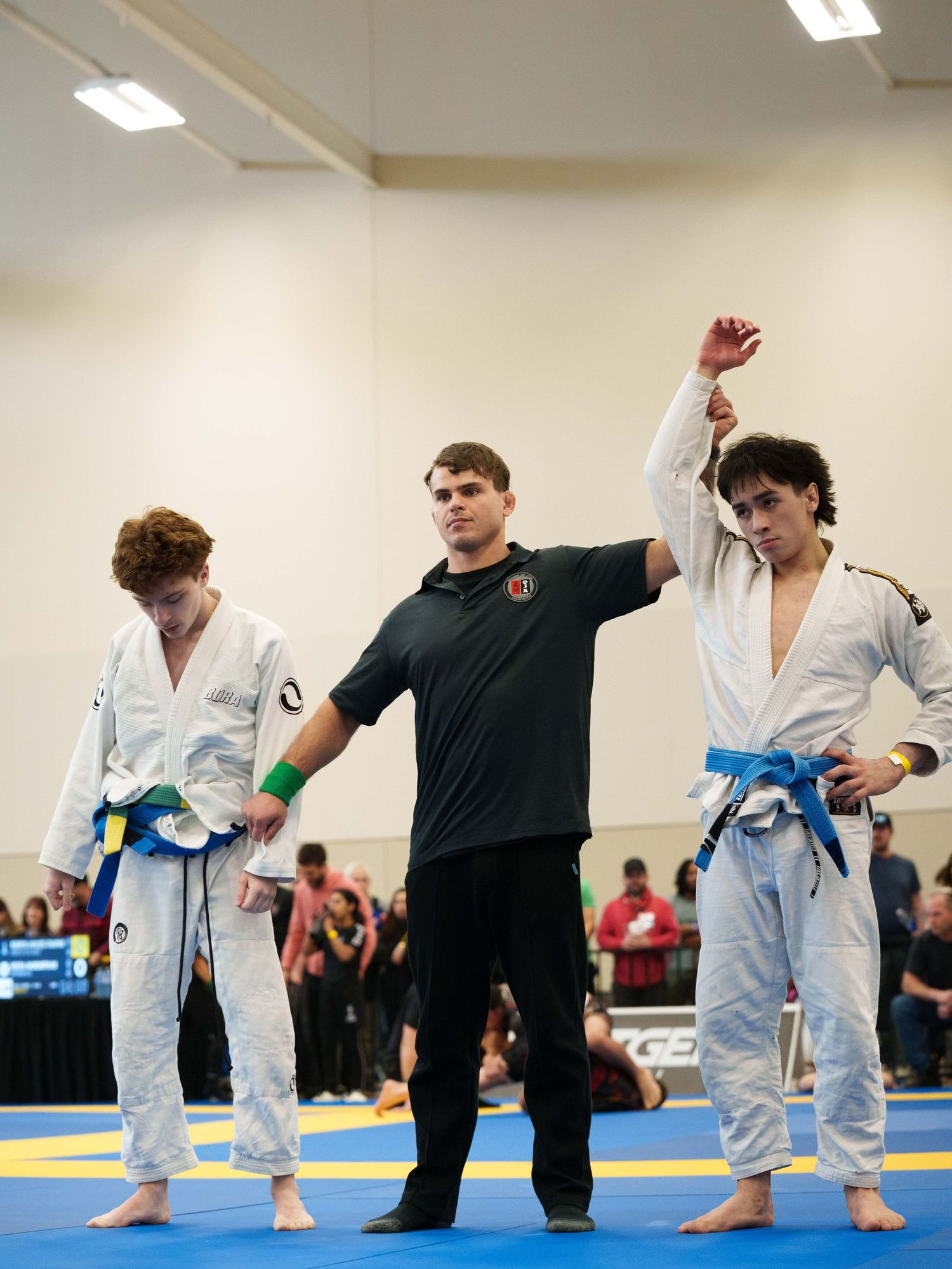 Two young boy BJJ fighters standing with a referee who holds one boy's arm up in victory.