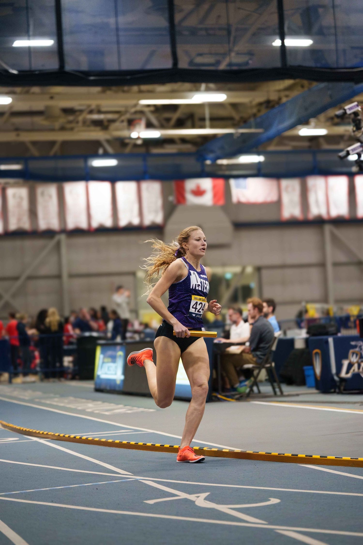 A young female relay runner running in front of a majestic background featuring the Canadian flag.