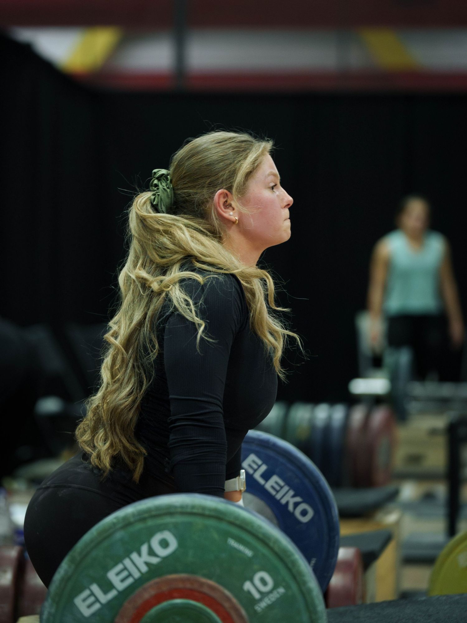 A young white female weightlifter with long wavy blonde hair gets ready to block pull.