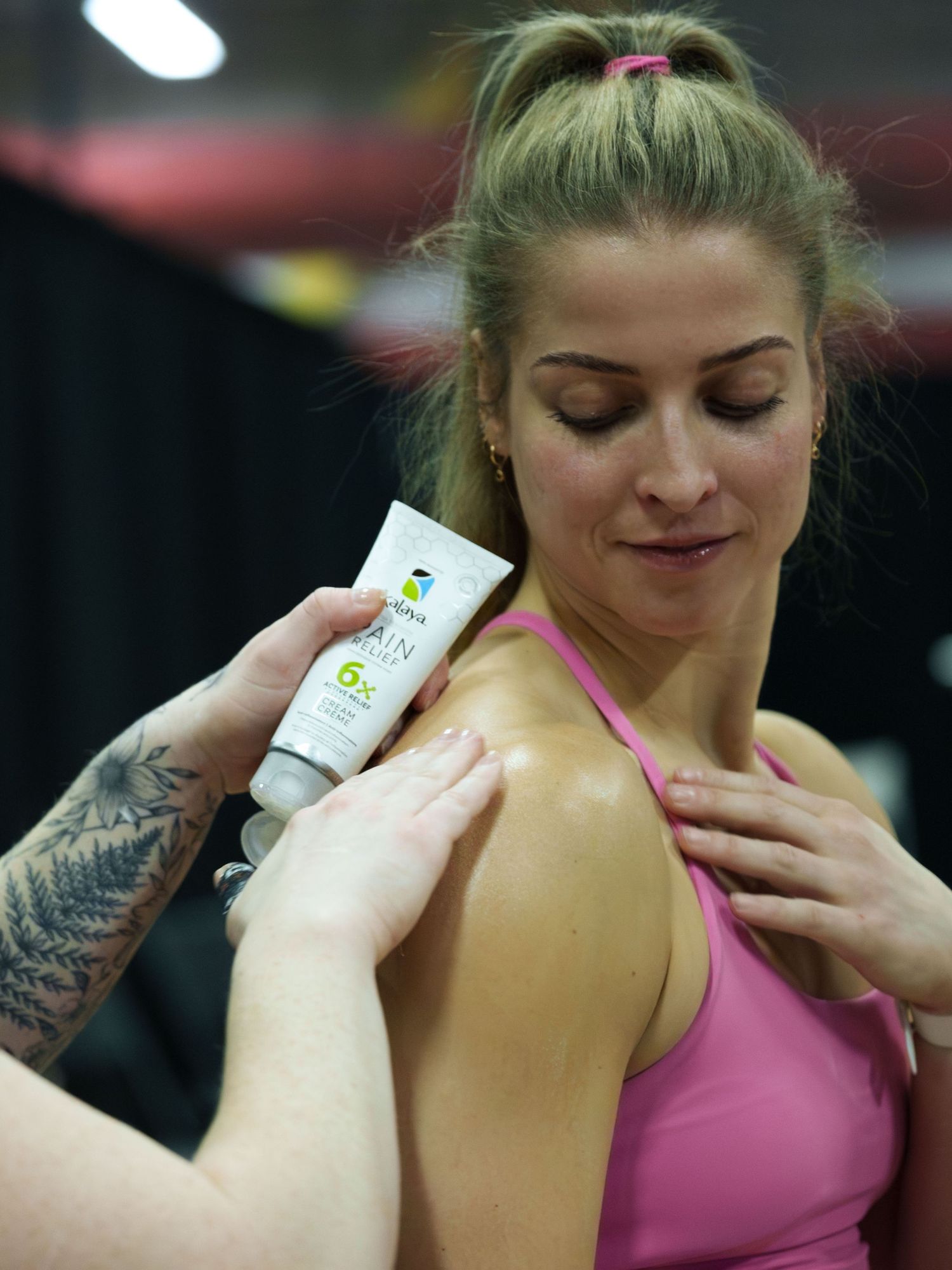 Product photography for a tube of pain relief cream. An anonymous woman applies the cream to the shoulder of a female athlete.