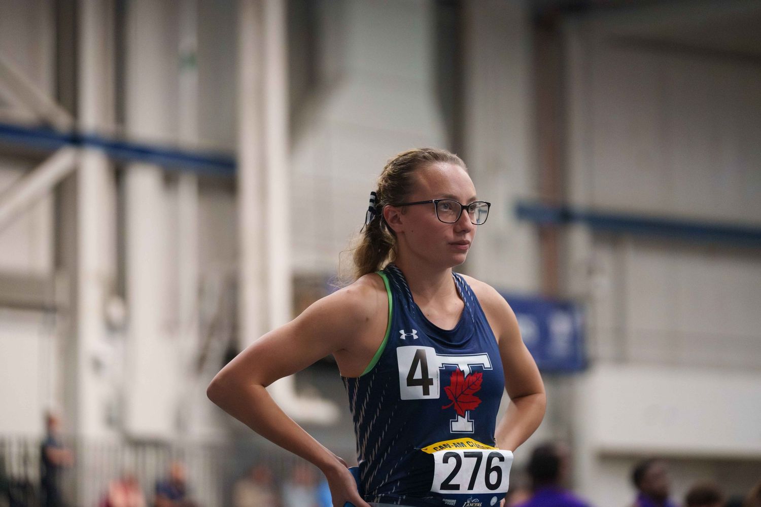 A young white female track runner stands focused at her starting block.