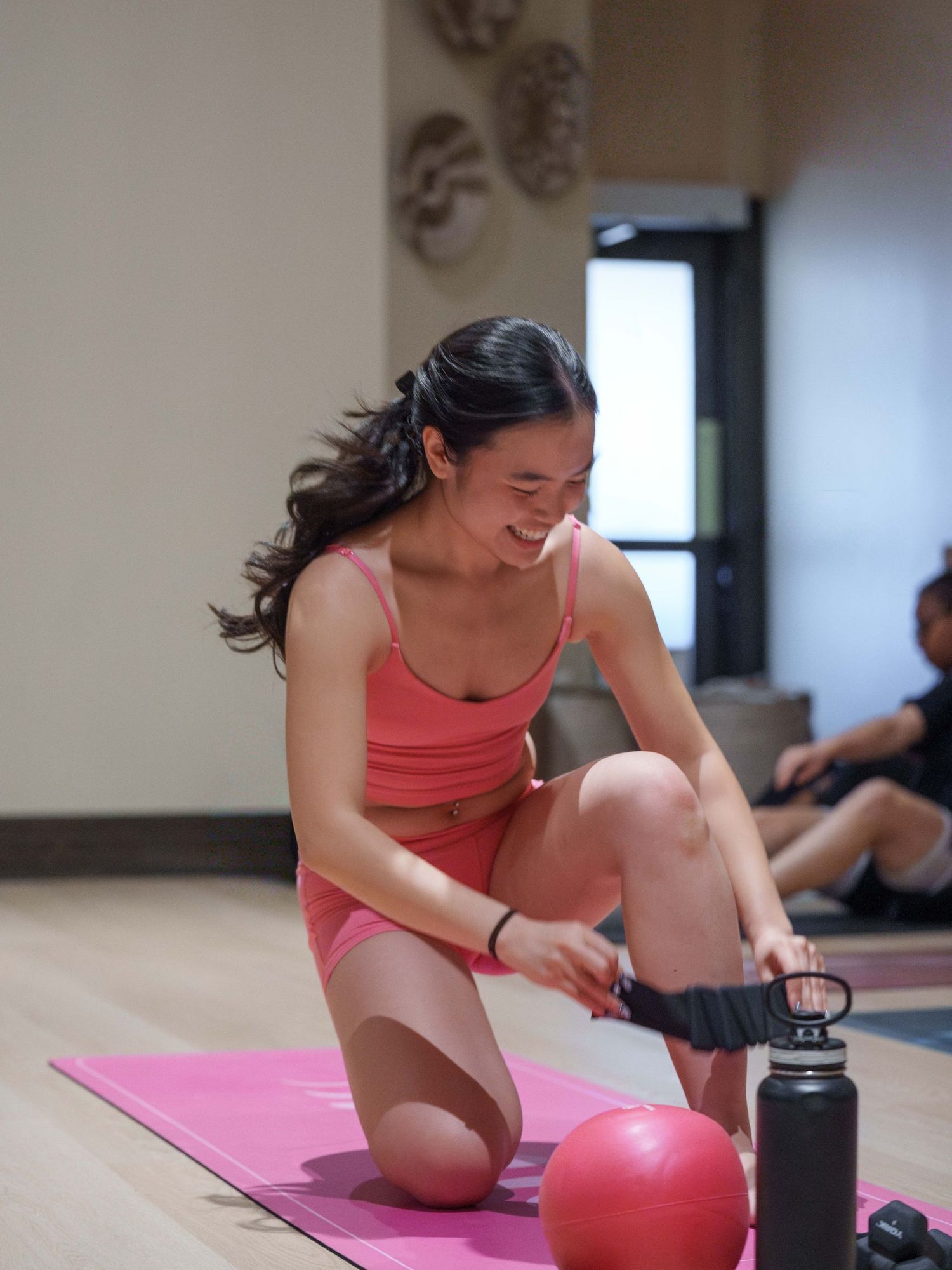 Brand photography for a pilates instructor teaching her pilates class. She wears a matching pink set and teaches atop a pink mat.