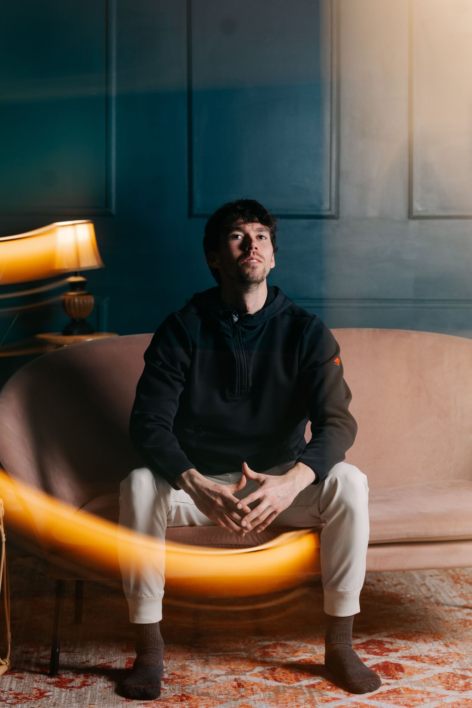 Flash studio portrait of a young white man sitting on a pink couch in front of a green wall being hit in the leg with a lamp motion blur.