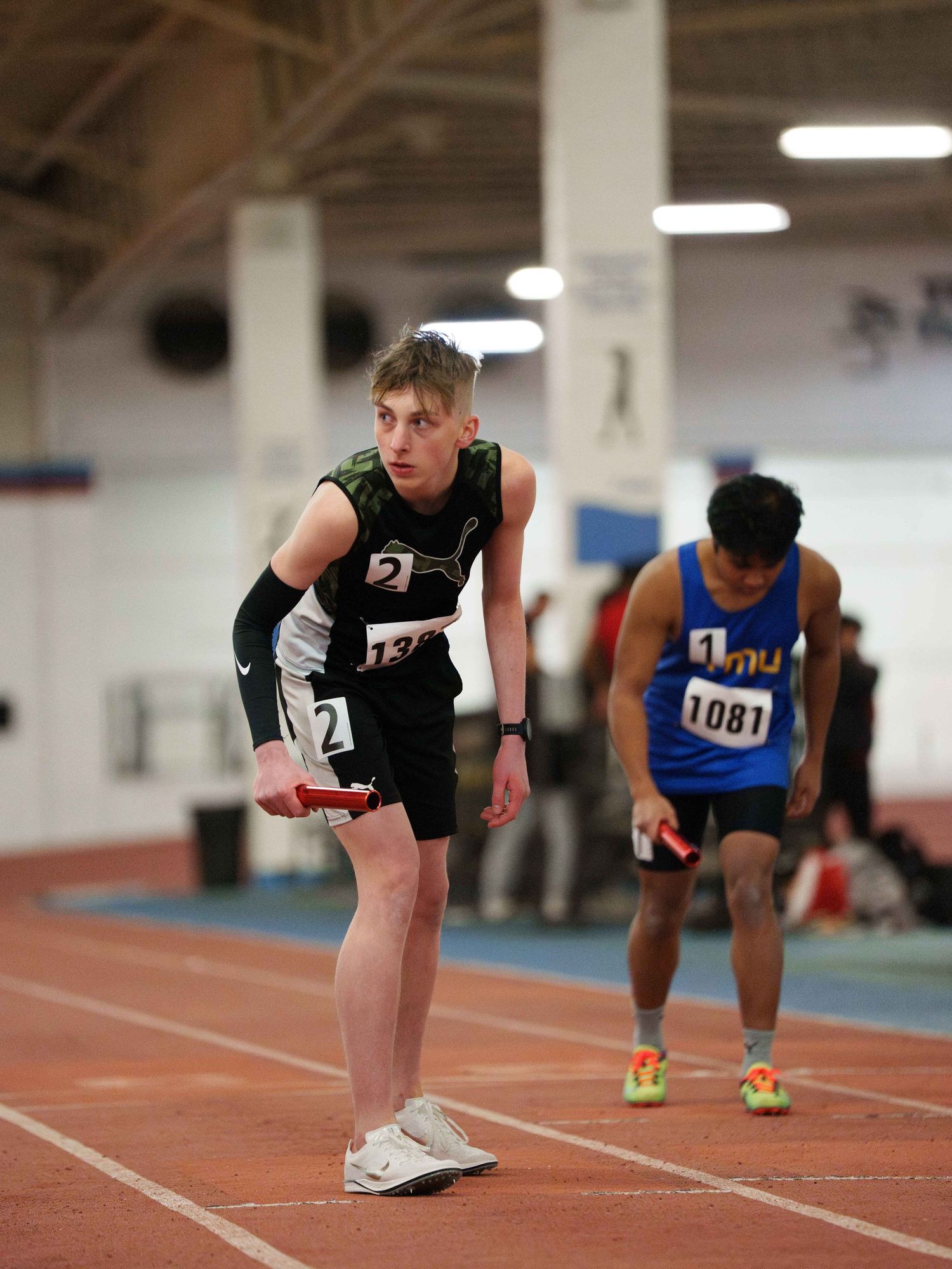 A young male track runner bent slightly over stares intensely with concentration towards the referee as he waits to begin his race.