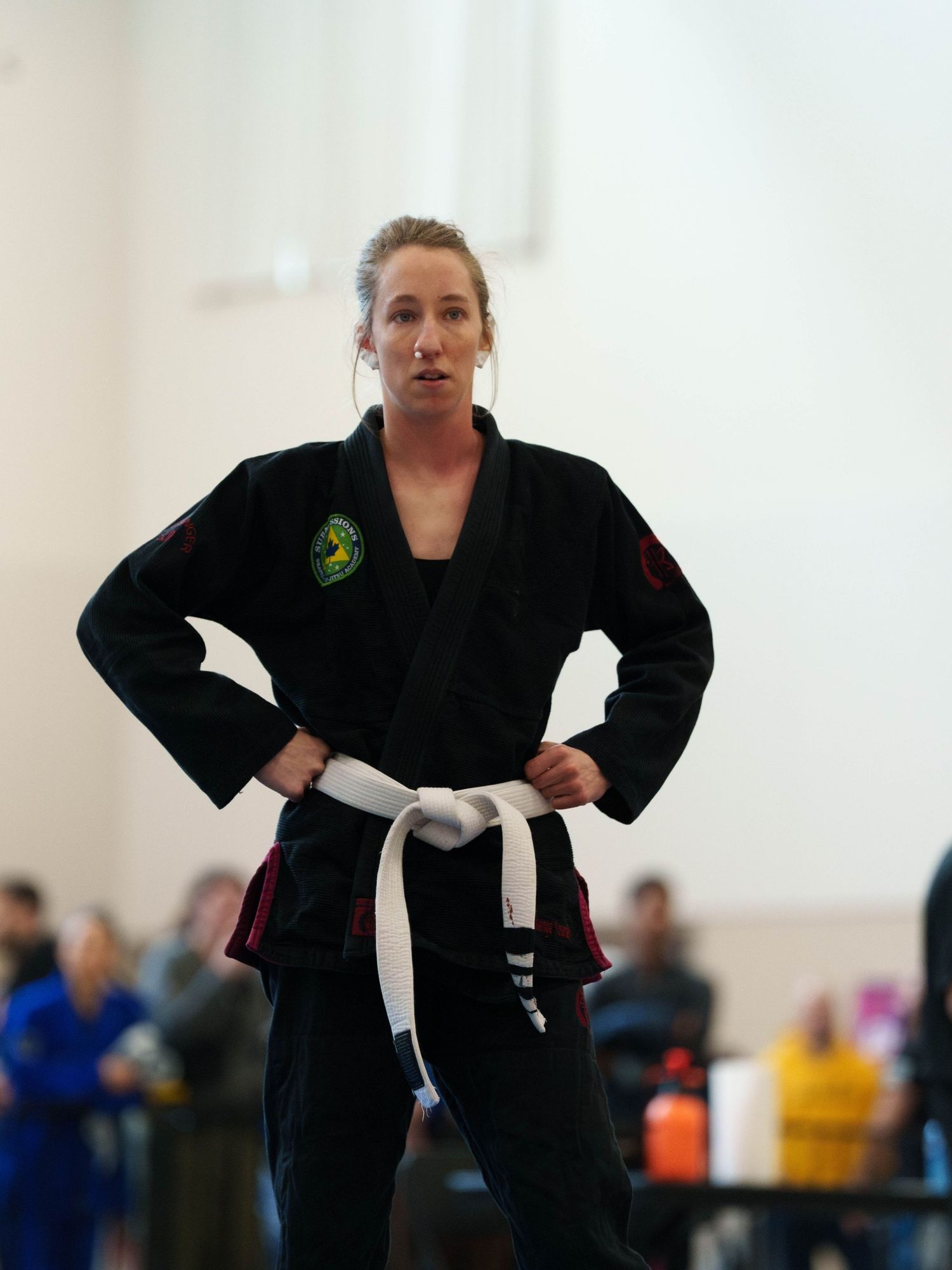 White female BJJ fighter stands contemplating her situation with tissue in her bloody nose.