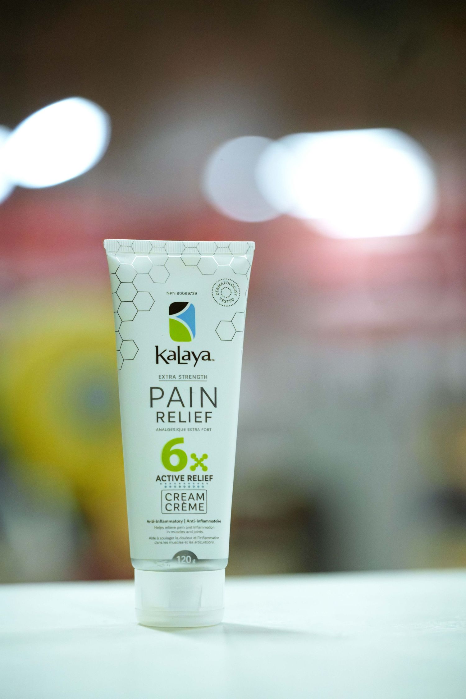 Product photo of a tube of pain relief cream set in front of a bright bokeh background. Tube reads 