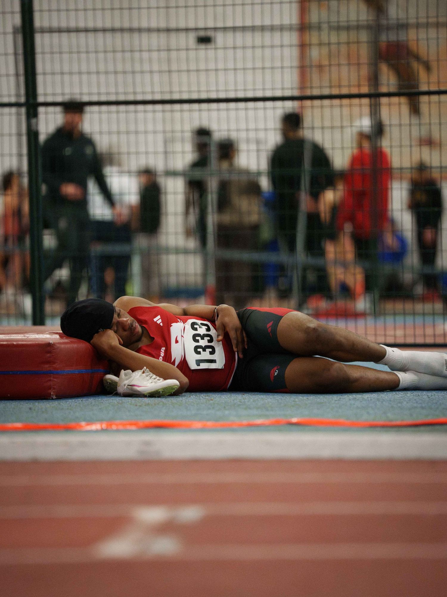 A young Black male track runner lies collapsed on his side on the track after a race.