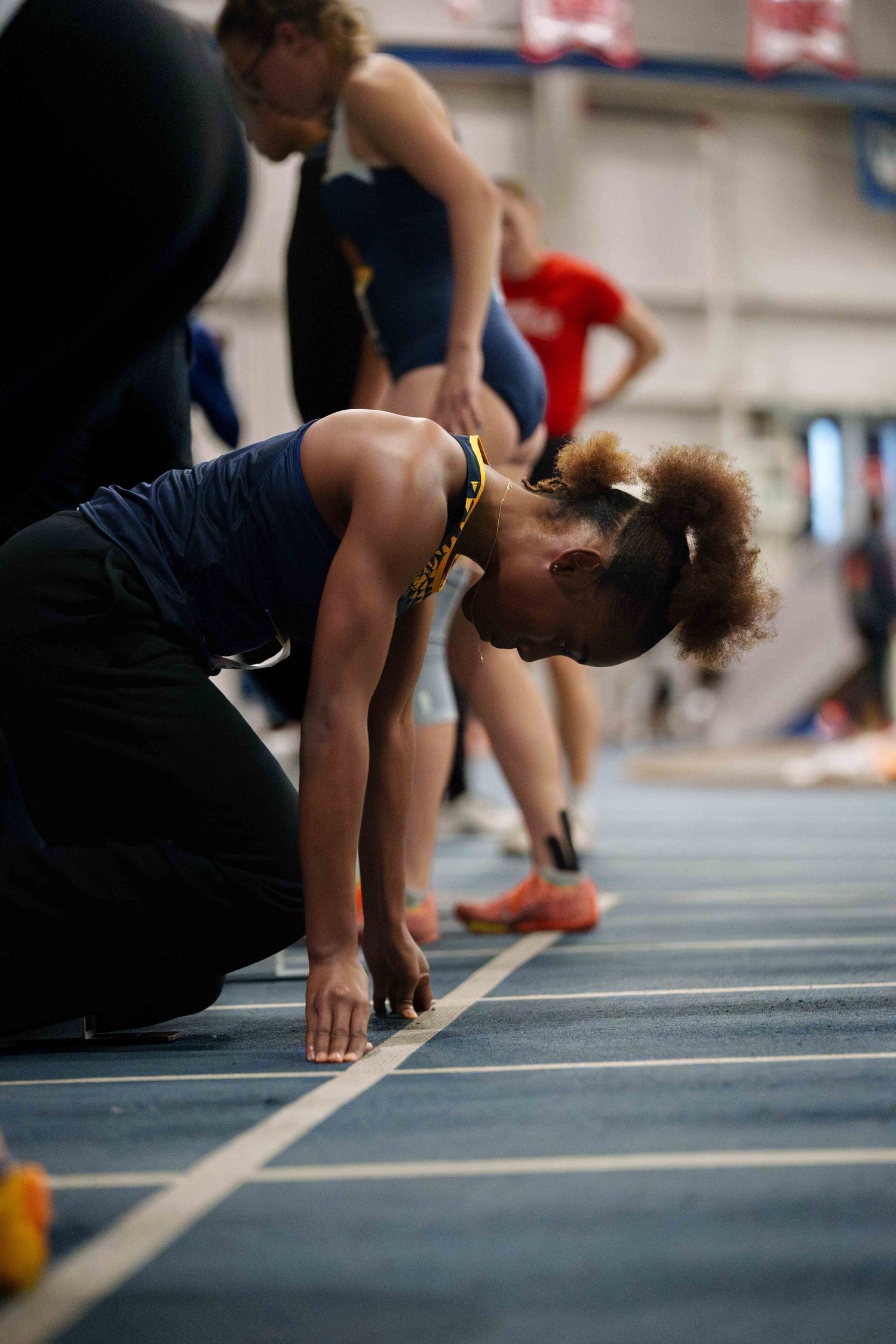 A young dark skinned female track runner in the starting sprint position at the starting line.