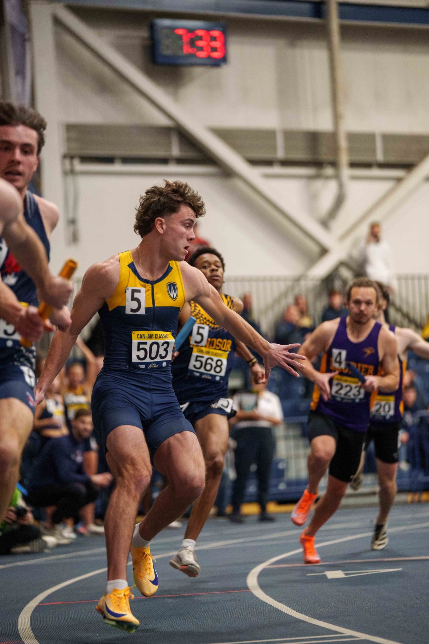 Male relay runners jockey for baton passes with intensely concentrated faces.
