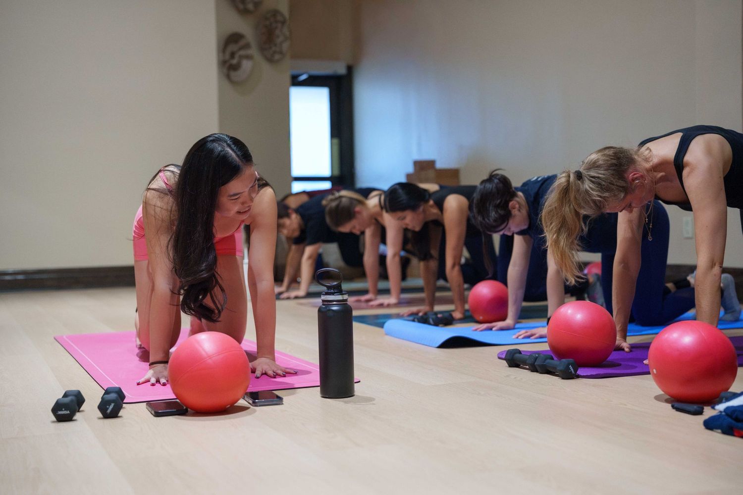 Brand photos of a pilates instructor teaching a pilates class. She wears a matching pink set and teaches atop a pink mat.