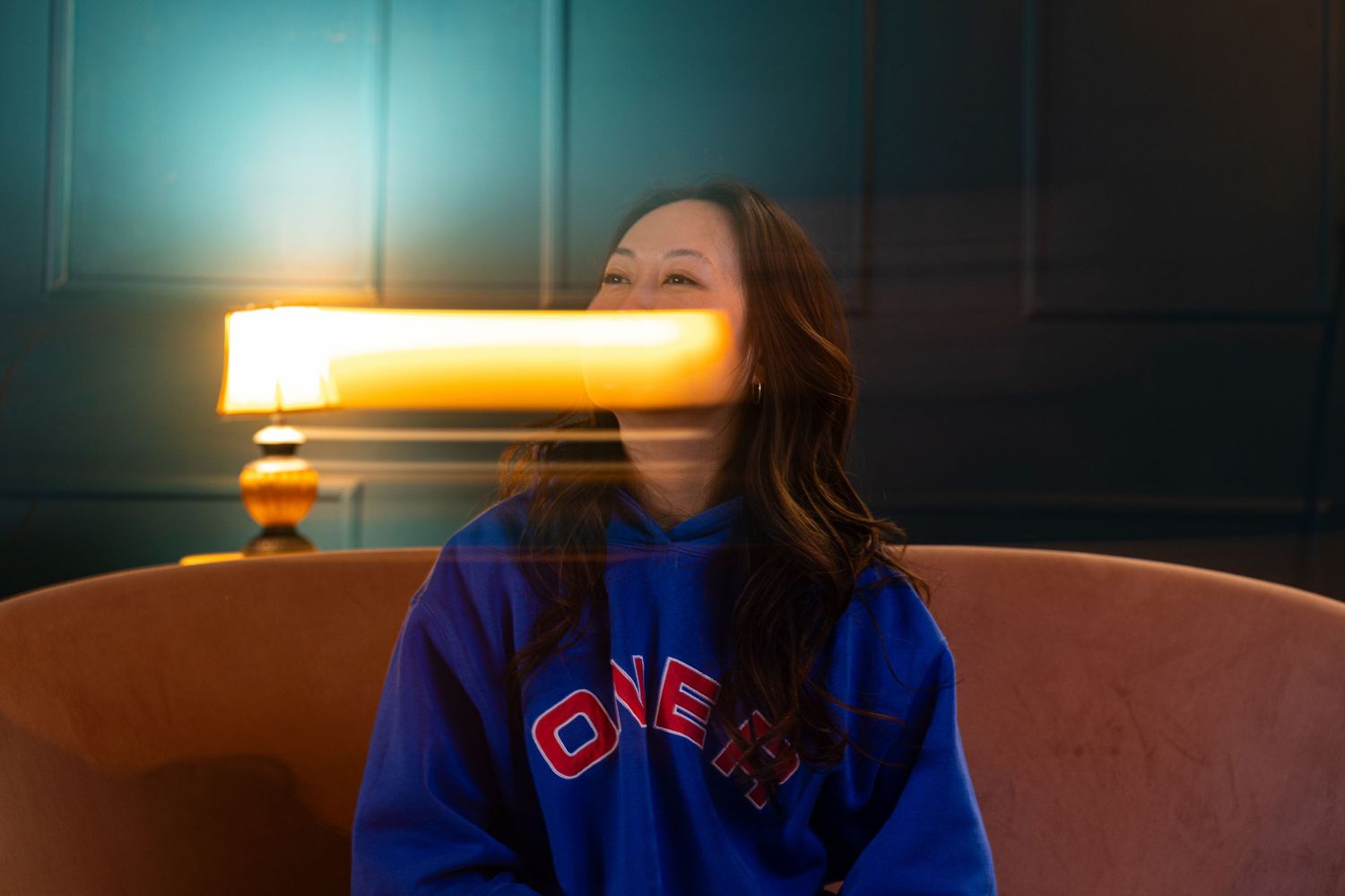 A creative motion blur portrait of a young adult Asian woman. She has wavy hair. A lamp motion blurs across the lower half of her face.