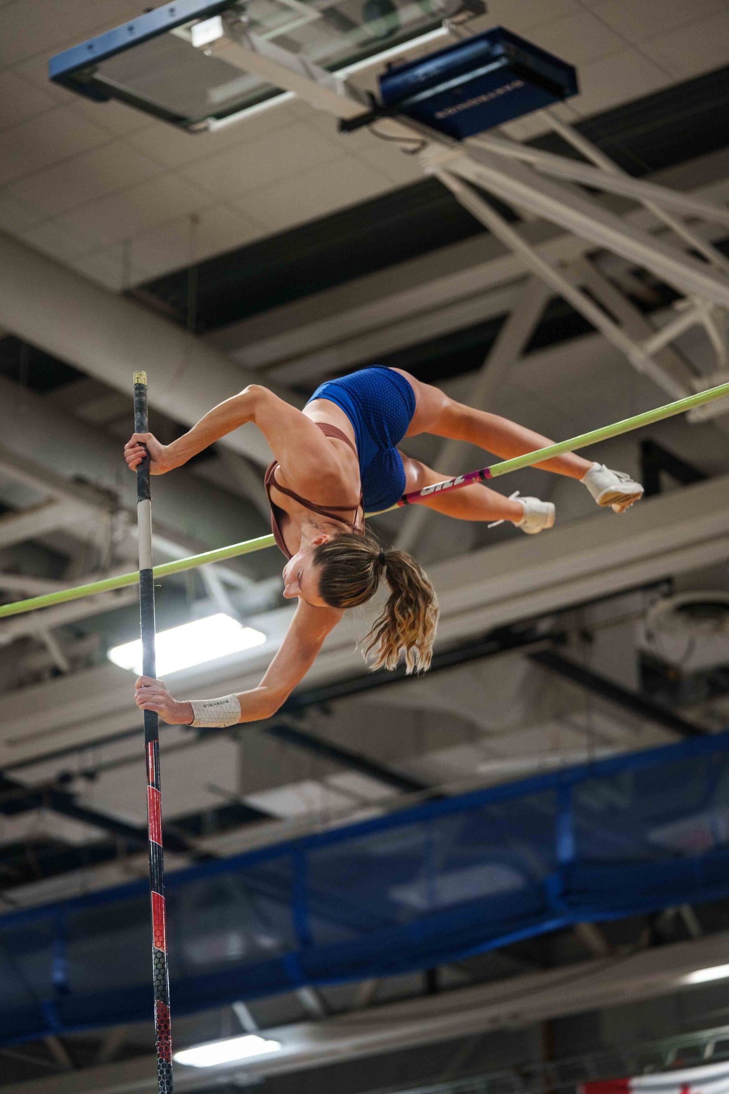 A tall female pole vaulter wrapped in mid-air around the bar.