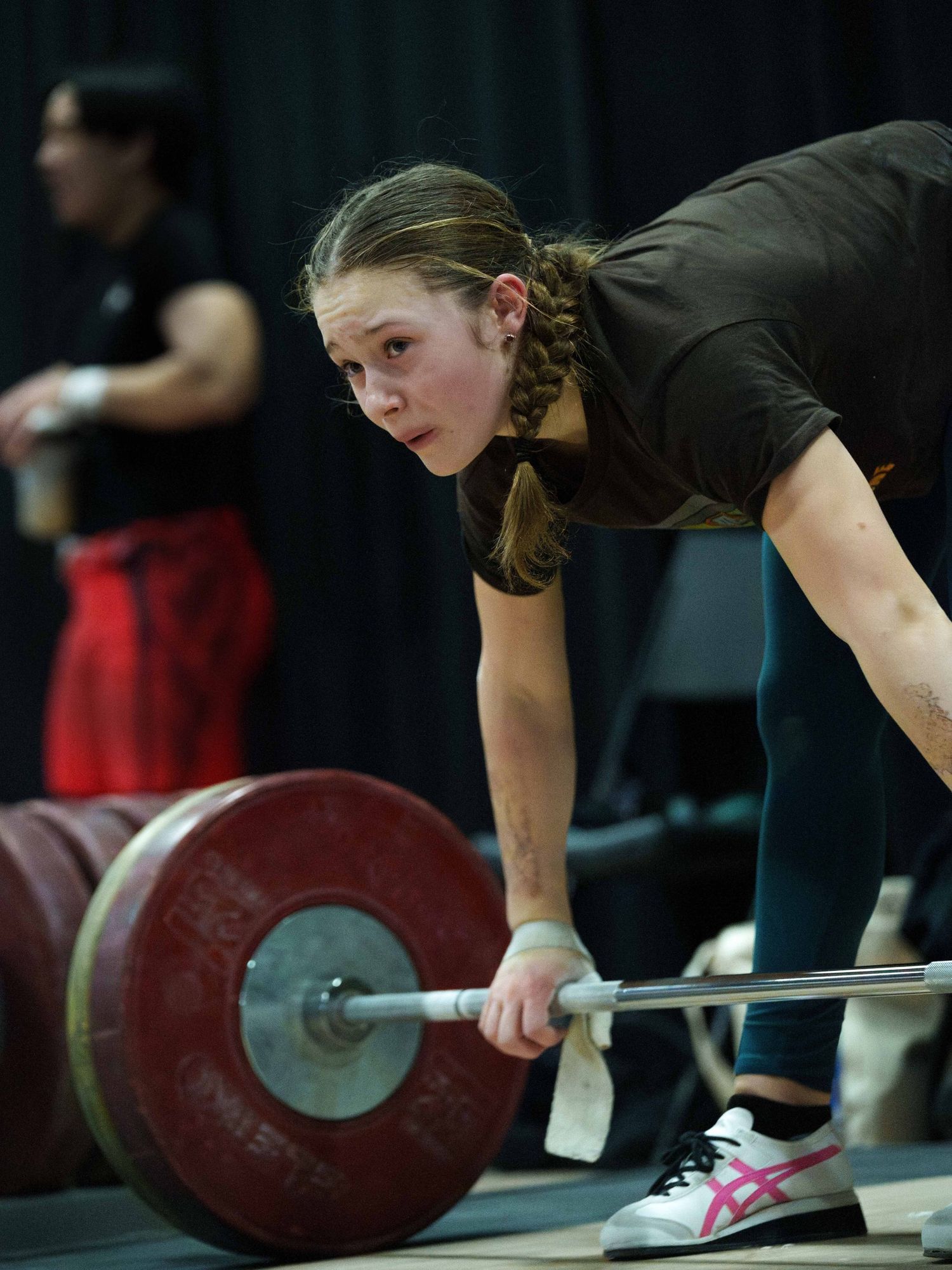 A young white female weightlifter looks tired at the bar before attempting a lift.