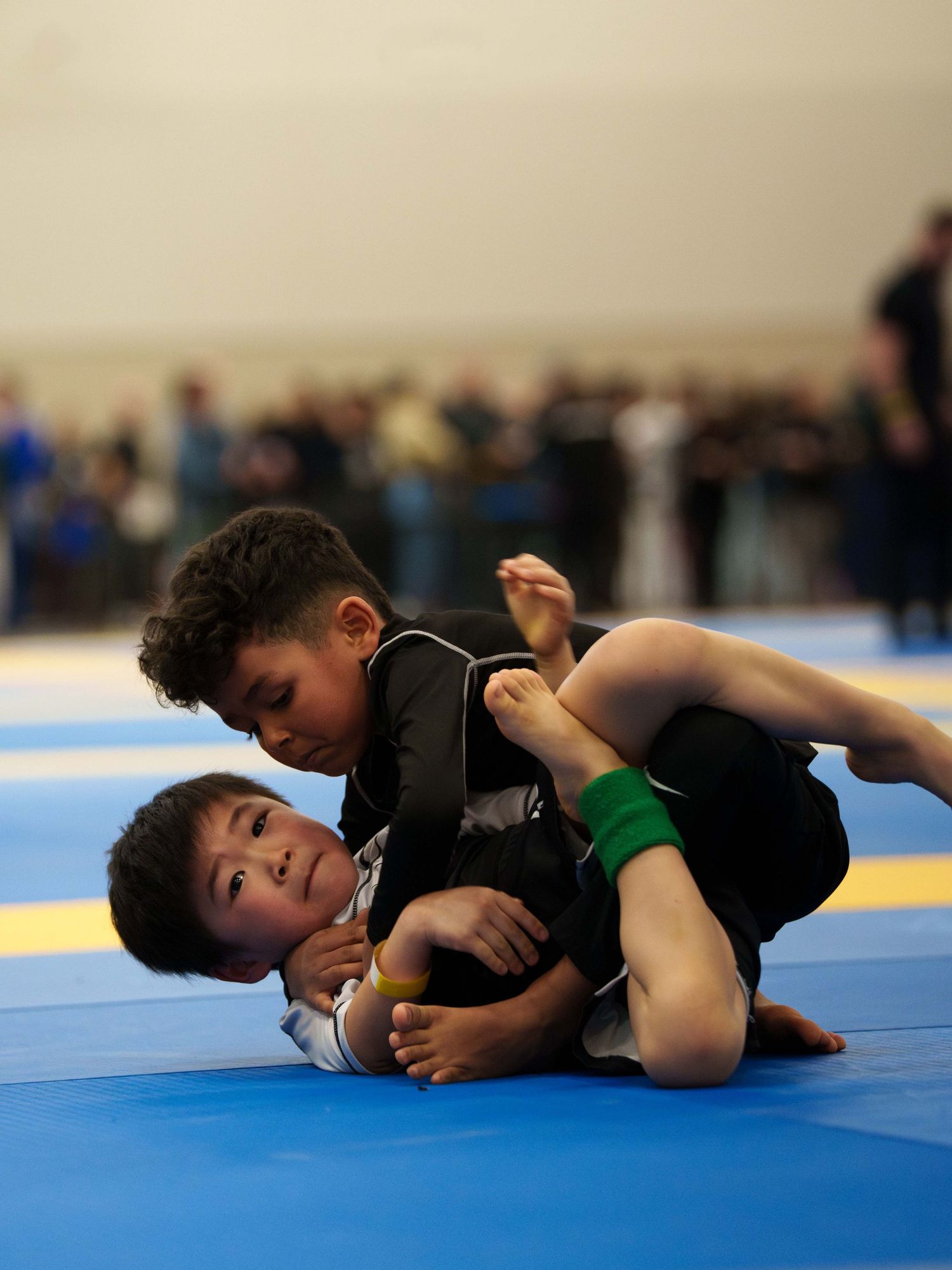 Two young boy BJJ fighters in rash guards grapple on the ground.