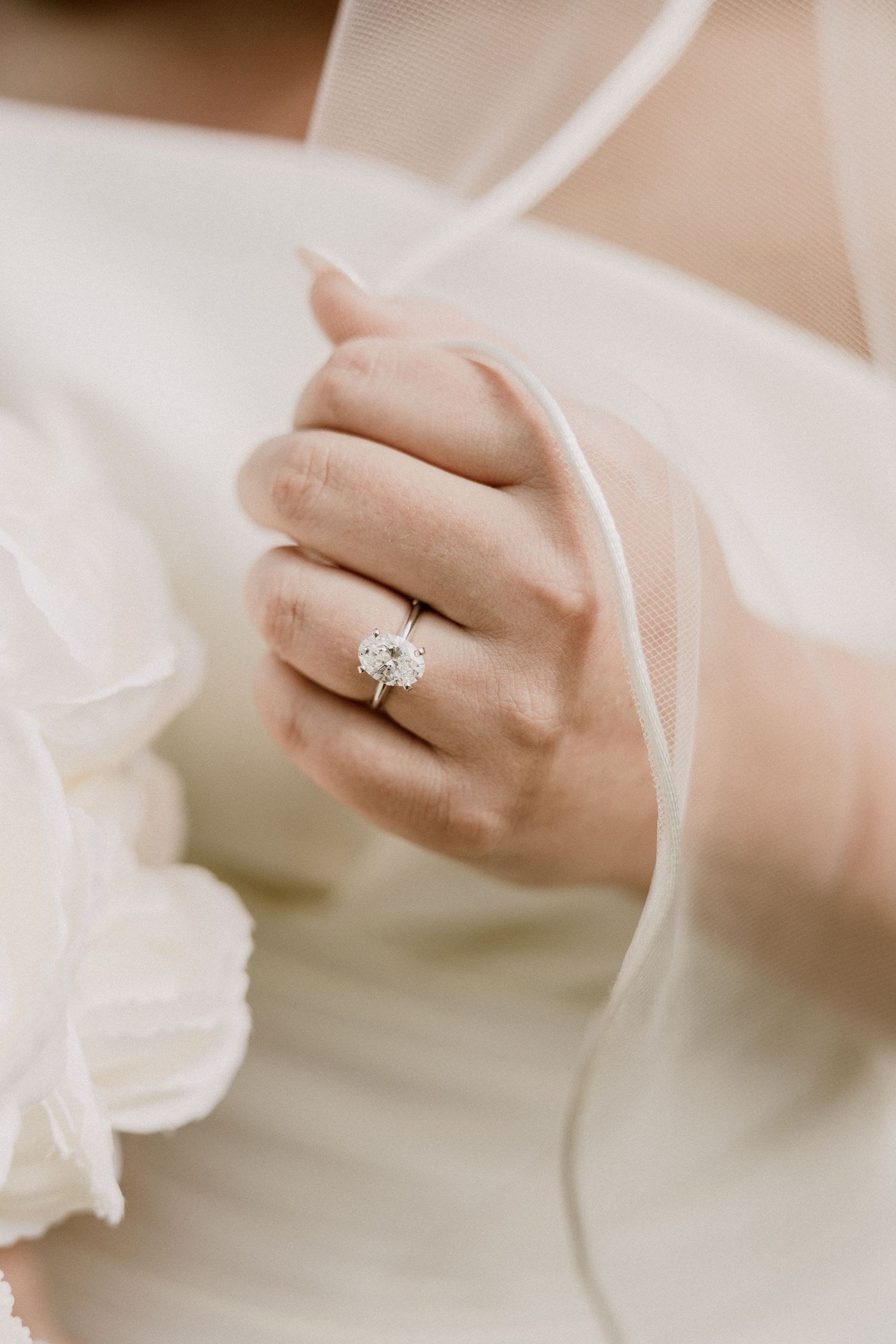 Close-up of a bride's hand wearing a stunning oval diamond solitaire engagement ring on her wedding day.