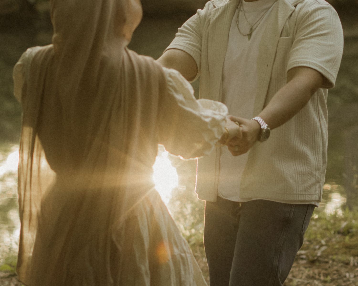 Couple holding hands at golden sunset in a dreamy outdoor setting, woman in flowing dress, warm backlit glow.