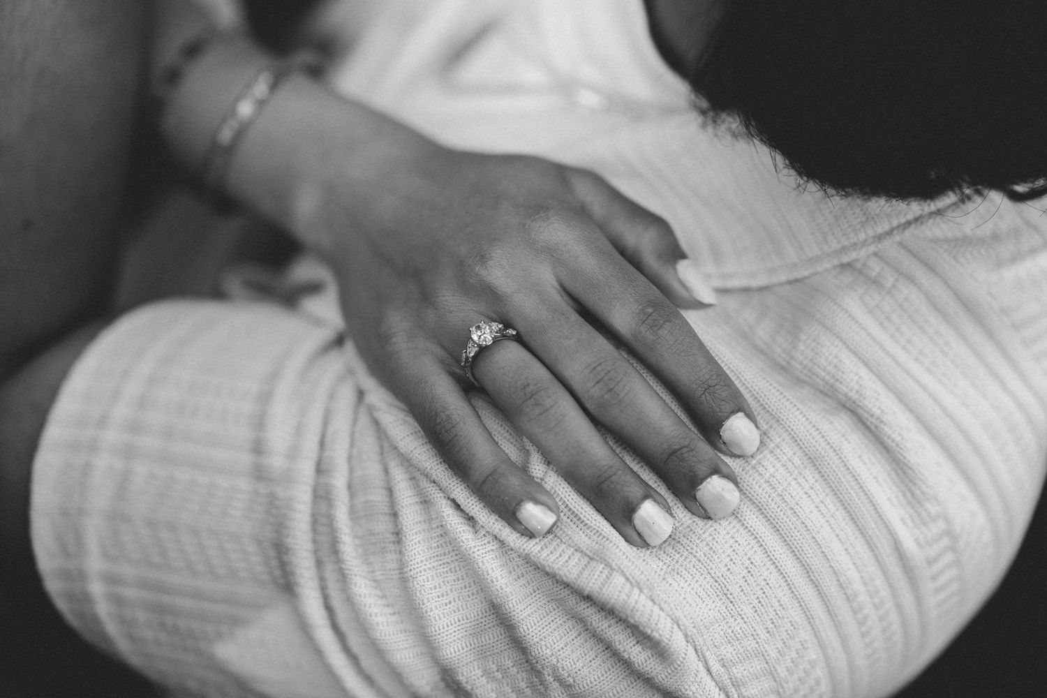 Black and white photo of a woman's hand with an engagement ring resting on a man's back.