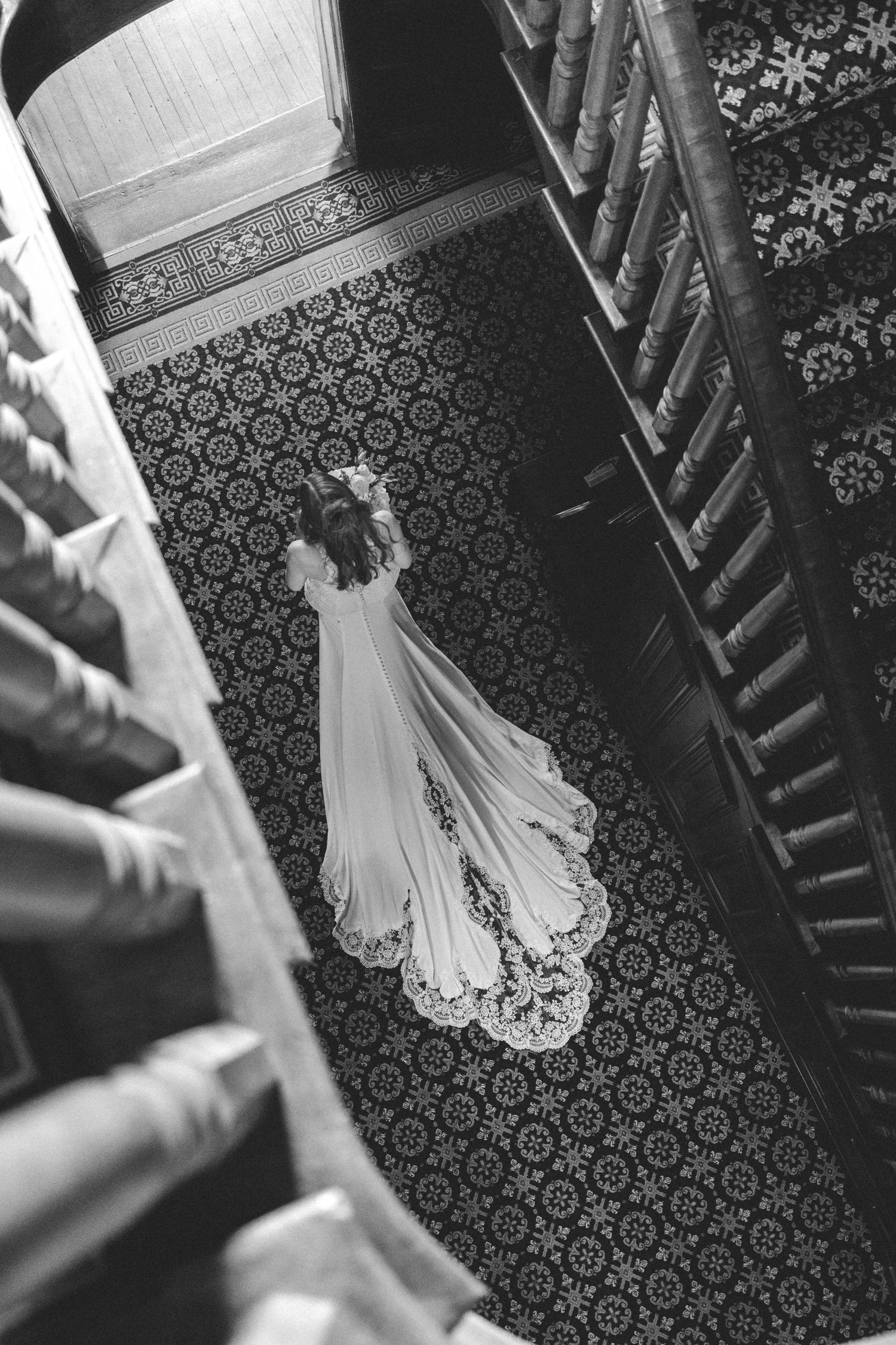 Aerial black and white photo of bride in lace wedding gown with train on ornate patterned floor.