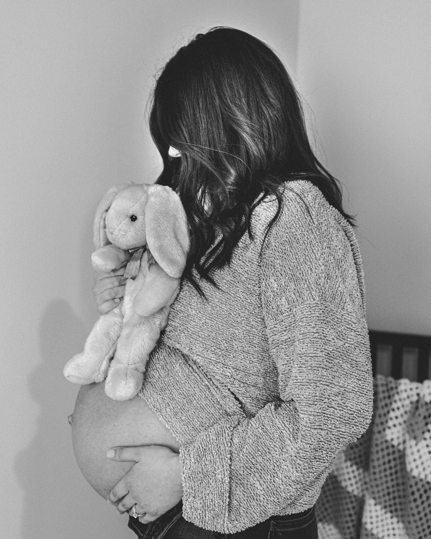Side view of pregnant woman in sweater holding stuffed bunny in black and white photo.
