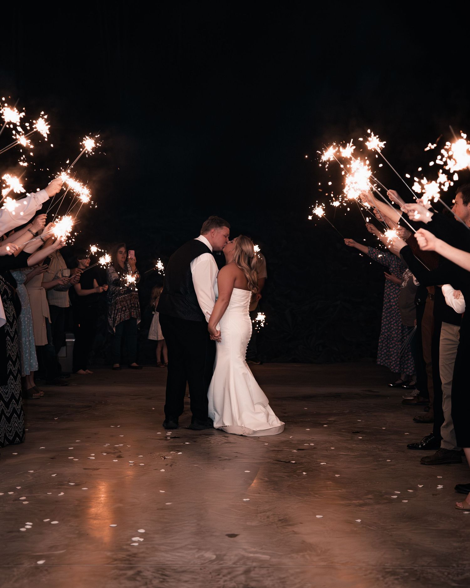 Bride and groom share a kiss during a romantic sparkler exit at their outdoor nighttime wedding celebration.