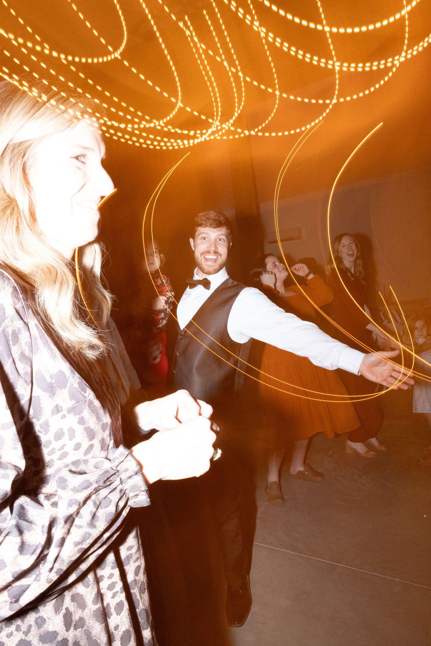 People dancing at an elegant party with warm golden string lights creating swirling bokeh effects in the background.