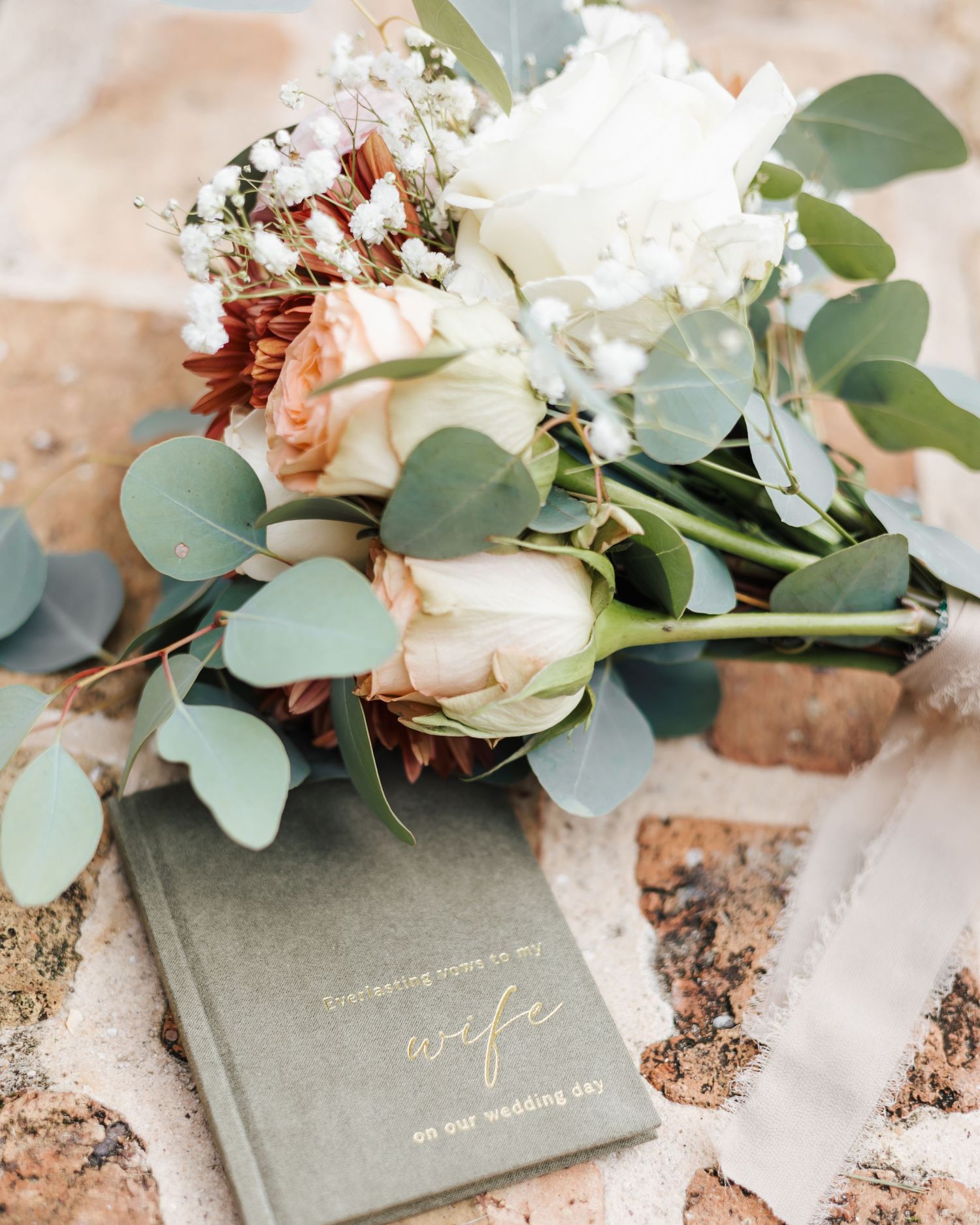 Elegant wedding vow books with gold lettering surrounded by delicate floral arrangements.