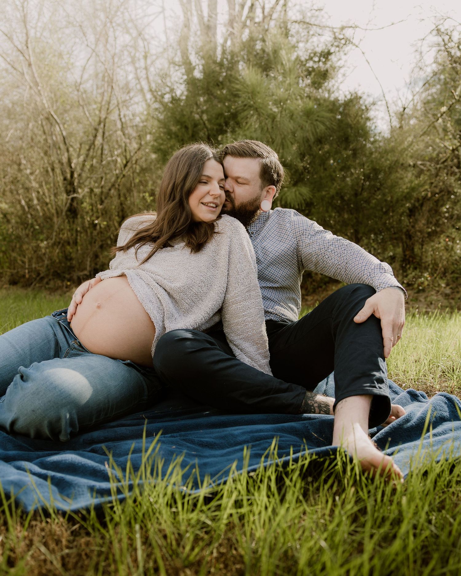 Couple cuddling on blue blanket during outdoor maternity session in natural setting.