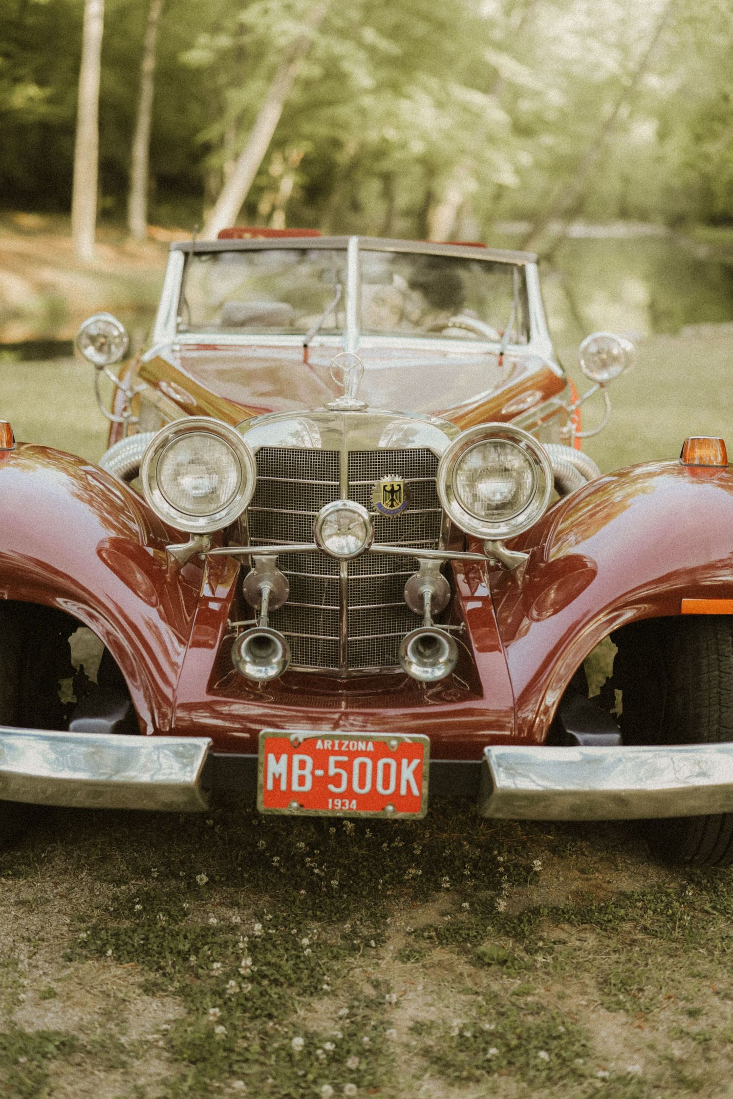 Vintage red classic car with Arizona license plate MB-500K parked outdoors, featuring chrome headlights and ornate grille.