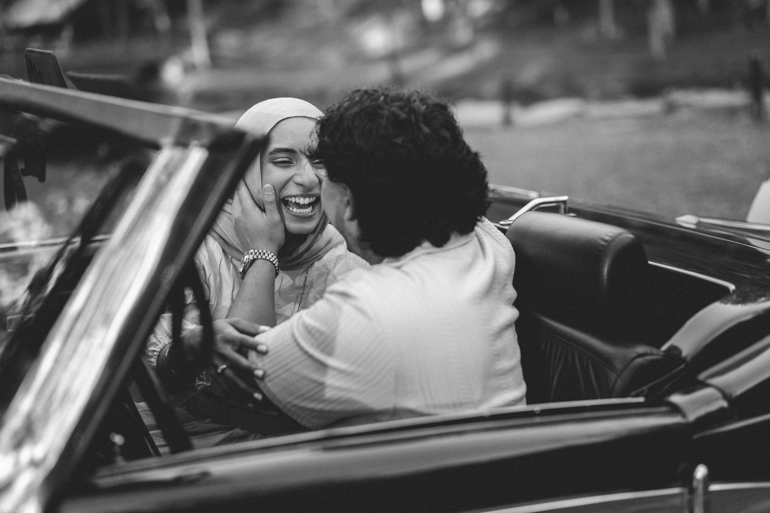 Black and white photo of two people laughing together in a classic convertible car.