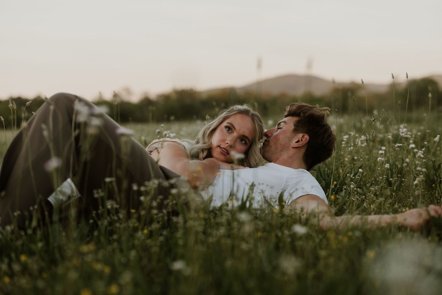A couple lying in a wildflower meadow, sharing a romantic moment at golden hour.