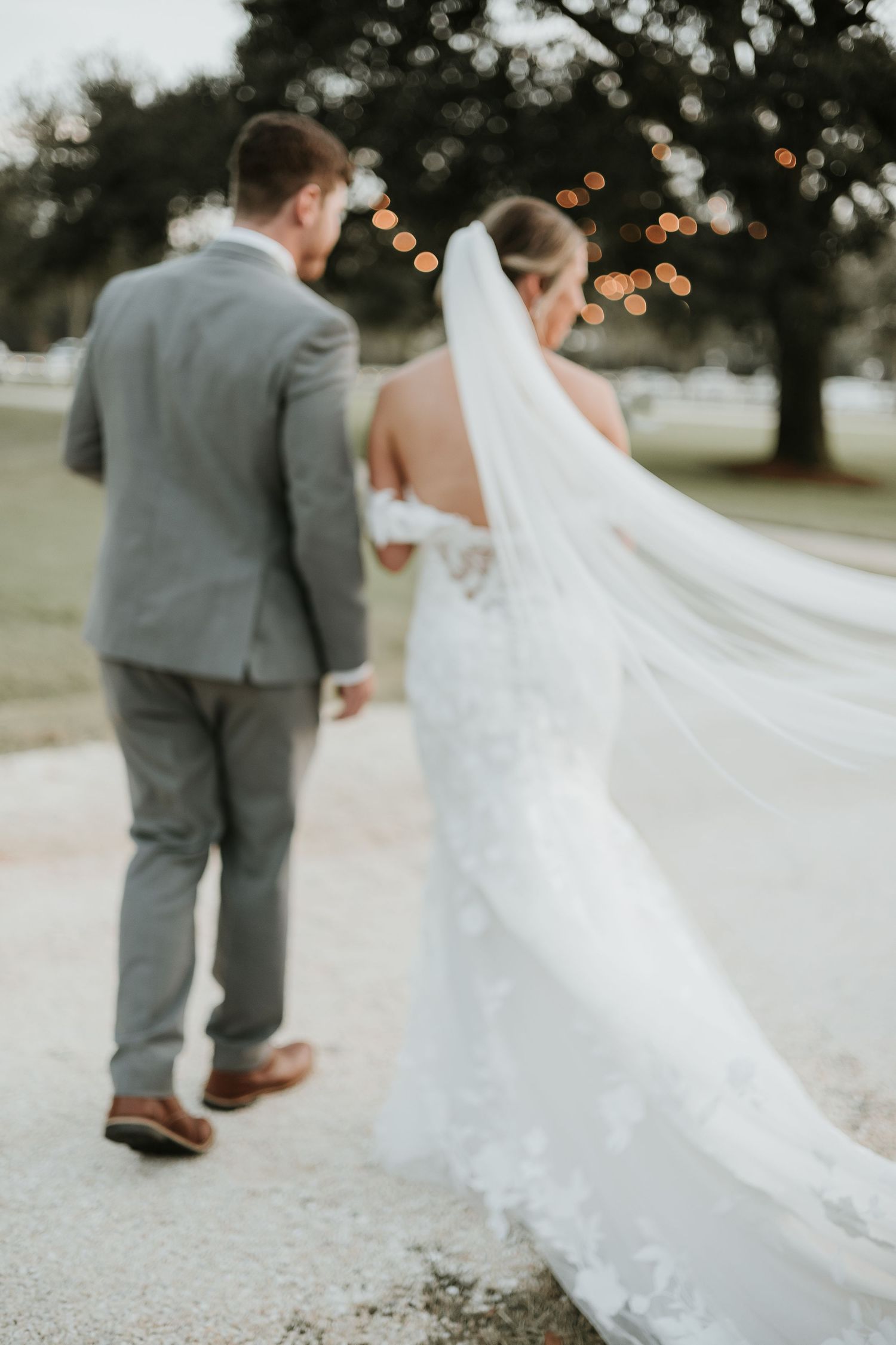 Wedding couple walking outdoors with flowing white veil trailing behind them.