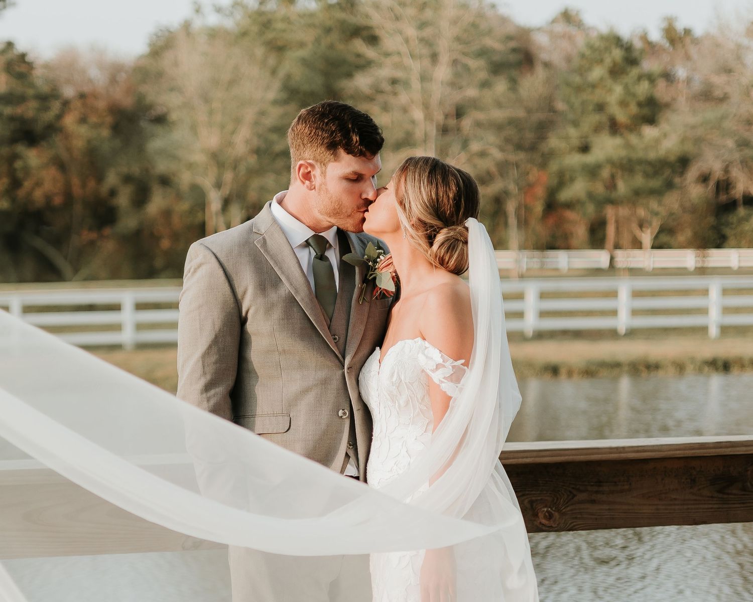 Elegant wedding couple embracing near white fence and water.