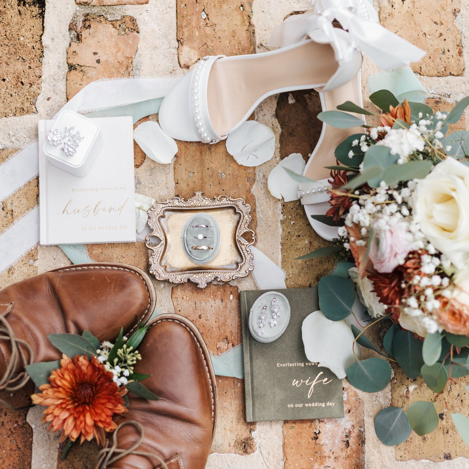Wedding details flat lay with leather accessories, flowers, and stationery on textured surface.