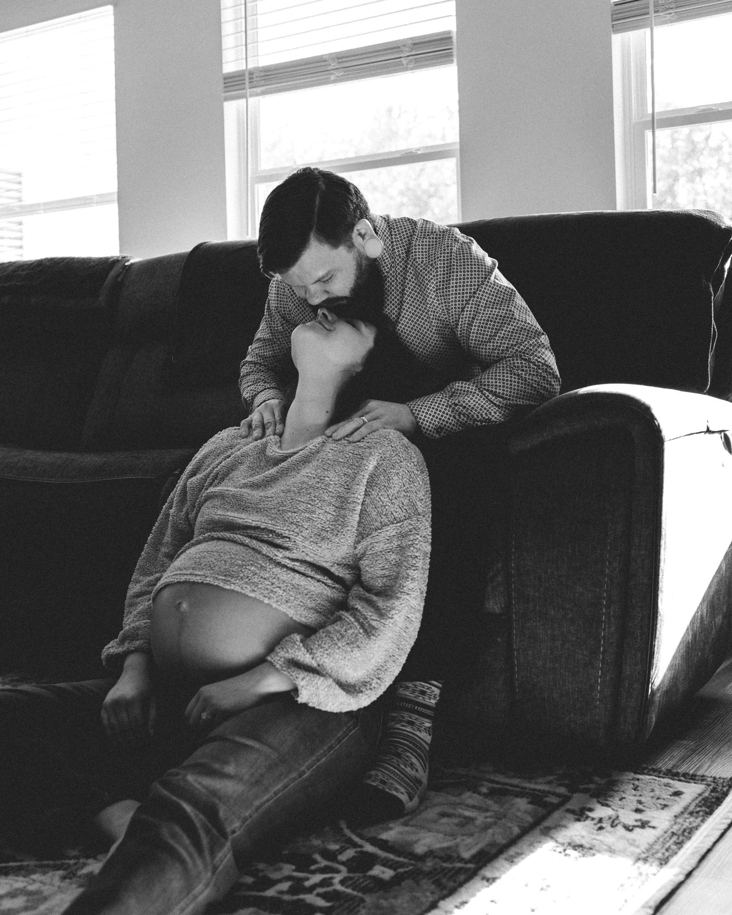 Black and white photo of couple sharing tender moment on dark couch.