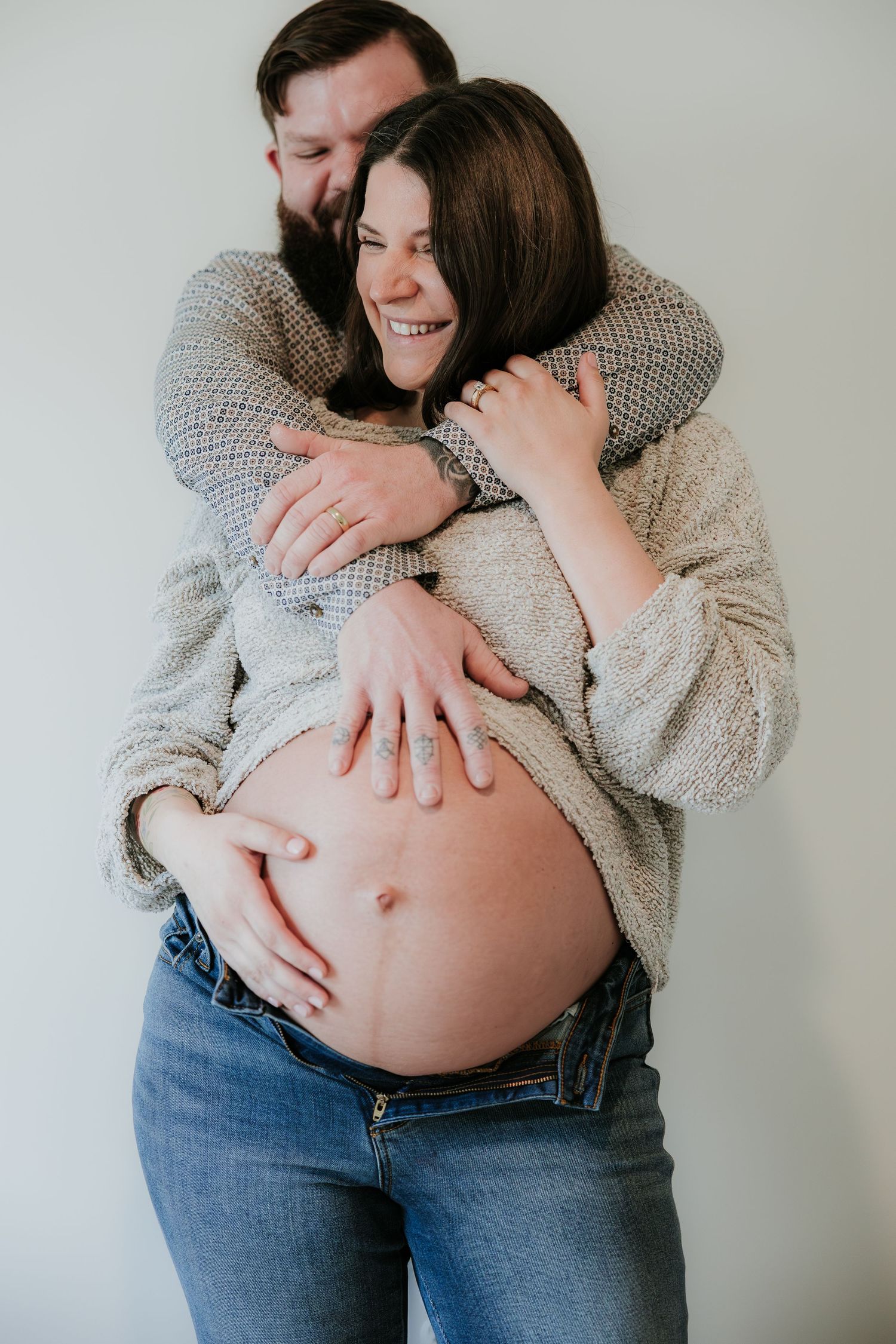 Intimate maternity photo showing couple embracing with hands on pregnant belly in cozy sweaters.