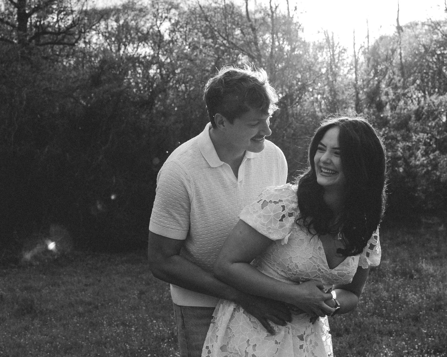 Black and white photo of a smiling couple embracing outdoors in a garden setting.