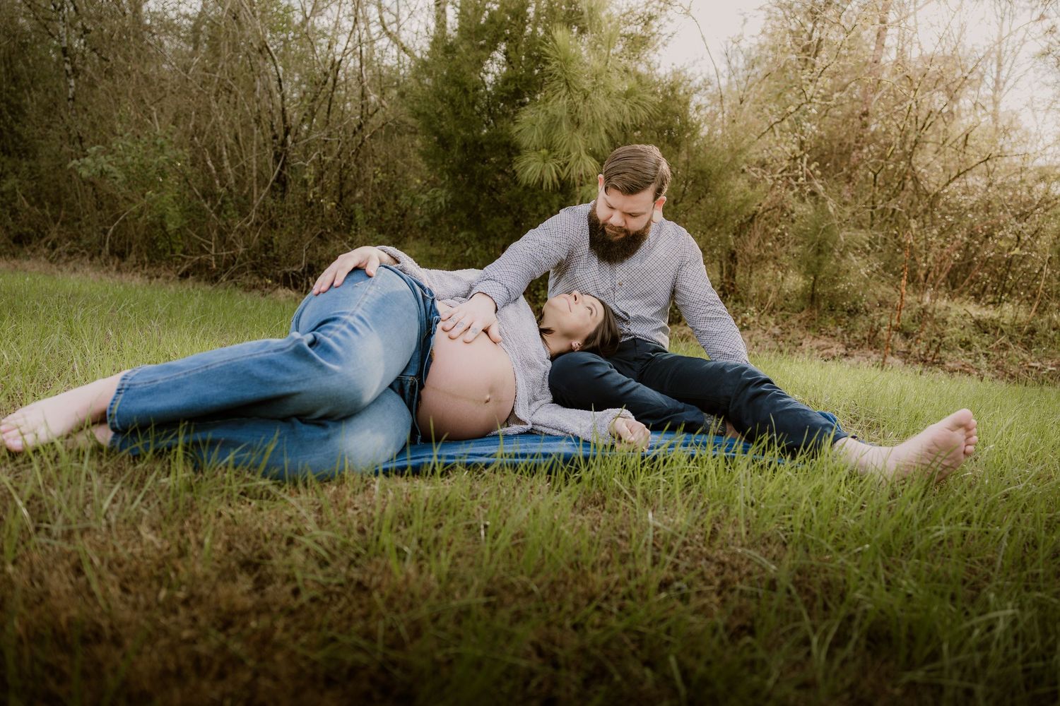 Couple shares tender moment during outdoor maternity session on blanket.