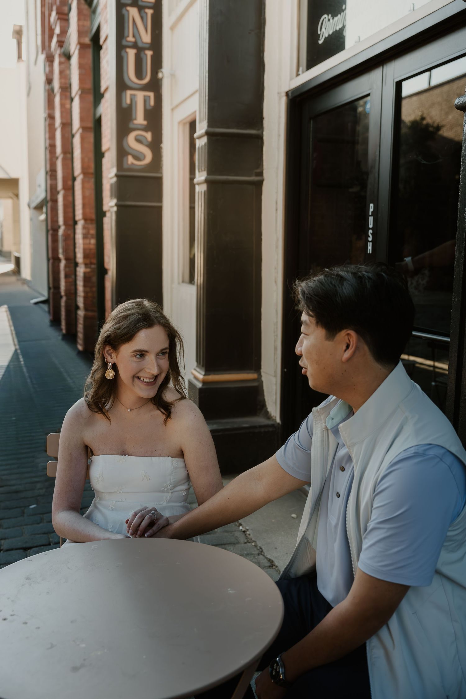 A couple sits together at a marble table in a restaurant, sharing an intimate conversation in natural light.