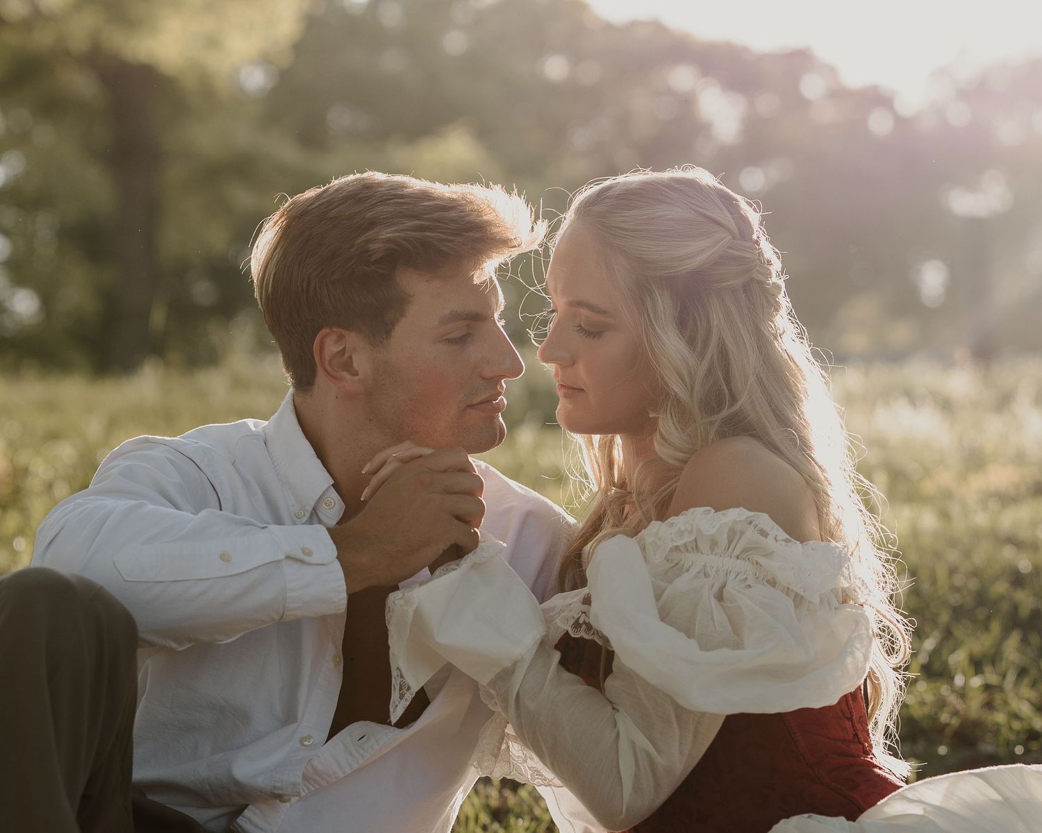 Romantic couple in vintage attire sharing a tender moment outdoors in golden sunlight.
