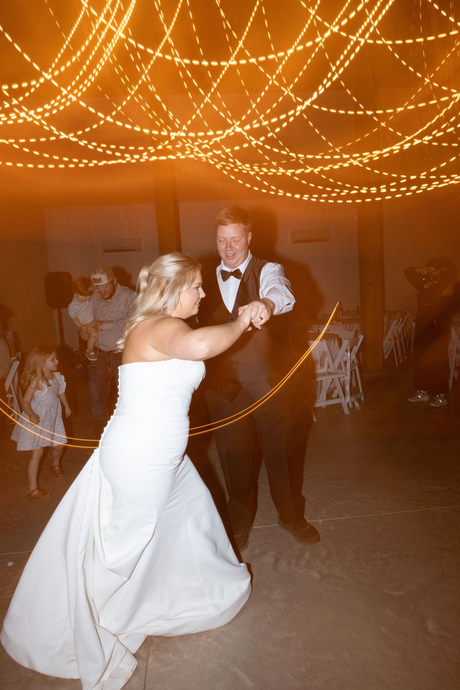 Bride and groom share their first dance under warm glowing string lights at an elegant wedding reception.