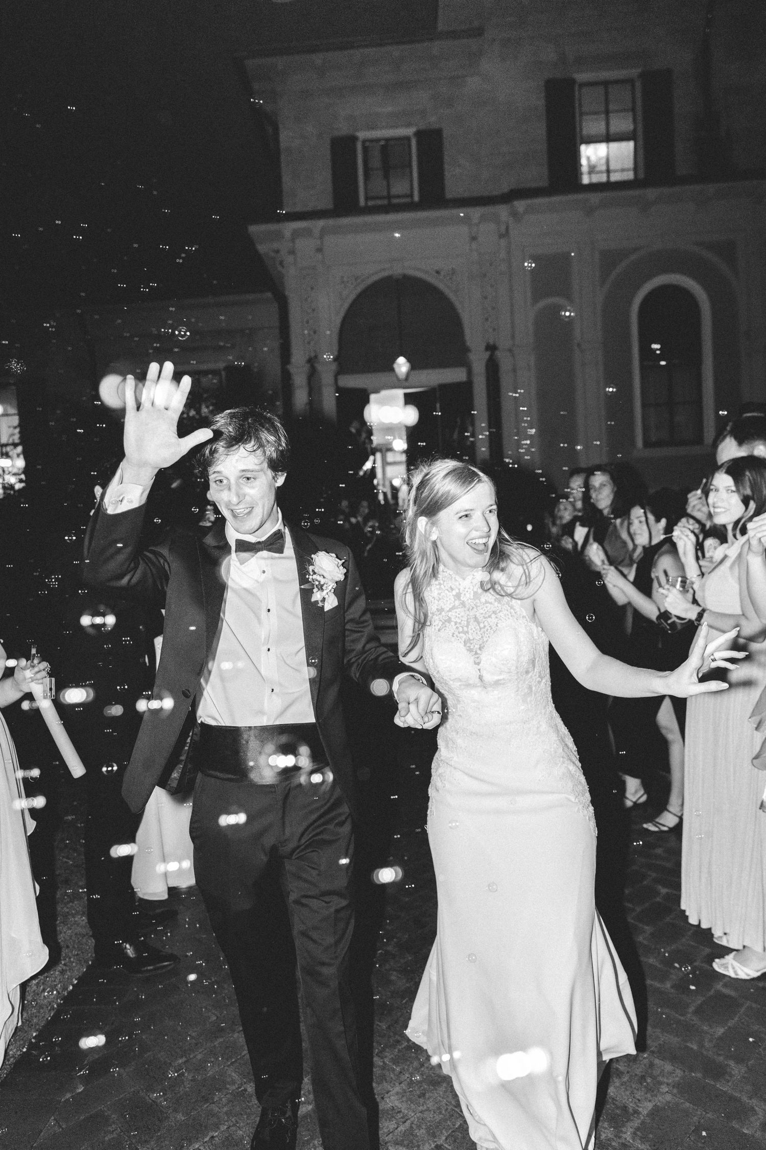 Black and white photo of a newlywed couple making a grand exit surrounded by bubbles at an elegant evening wedding.