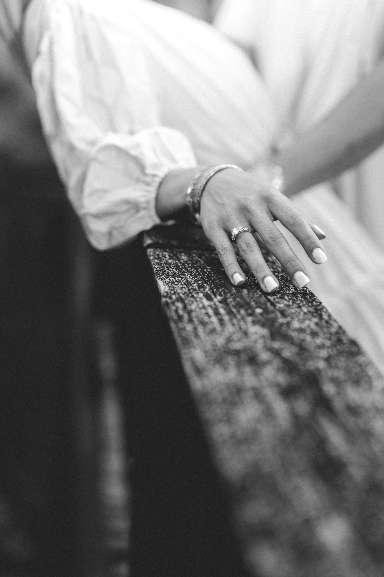 Black and white photo of a woman's hand with a ring and bracelet resting on a weathered wooden surface.