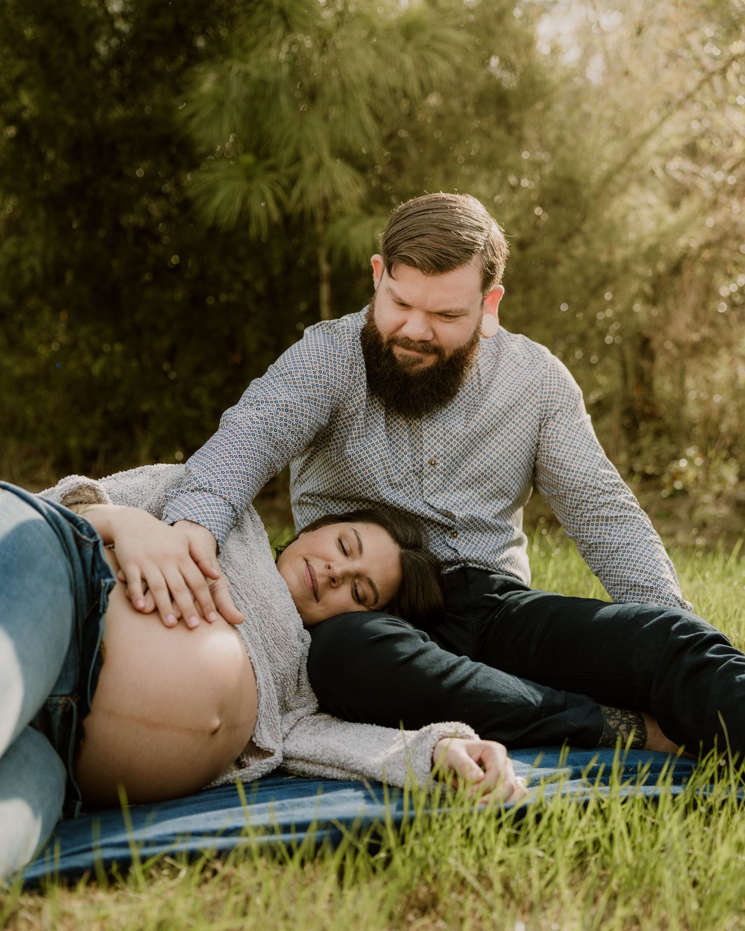 Expectant couple relaxing on blanket outdoors during maternity photoshoot.