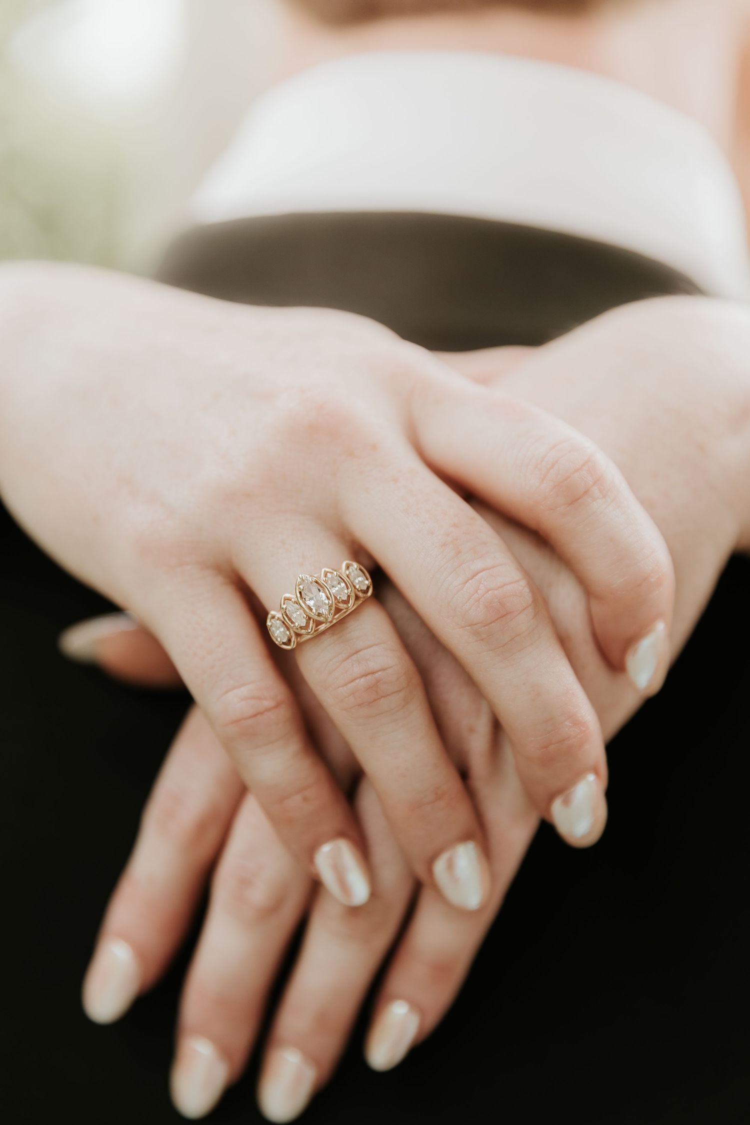 Close-up of hands wearing a gold multi-stone ring with pearl manicure, elegant bridal jewelry detail.