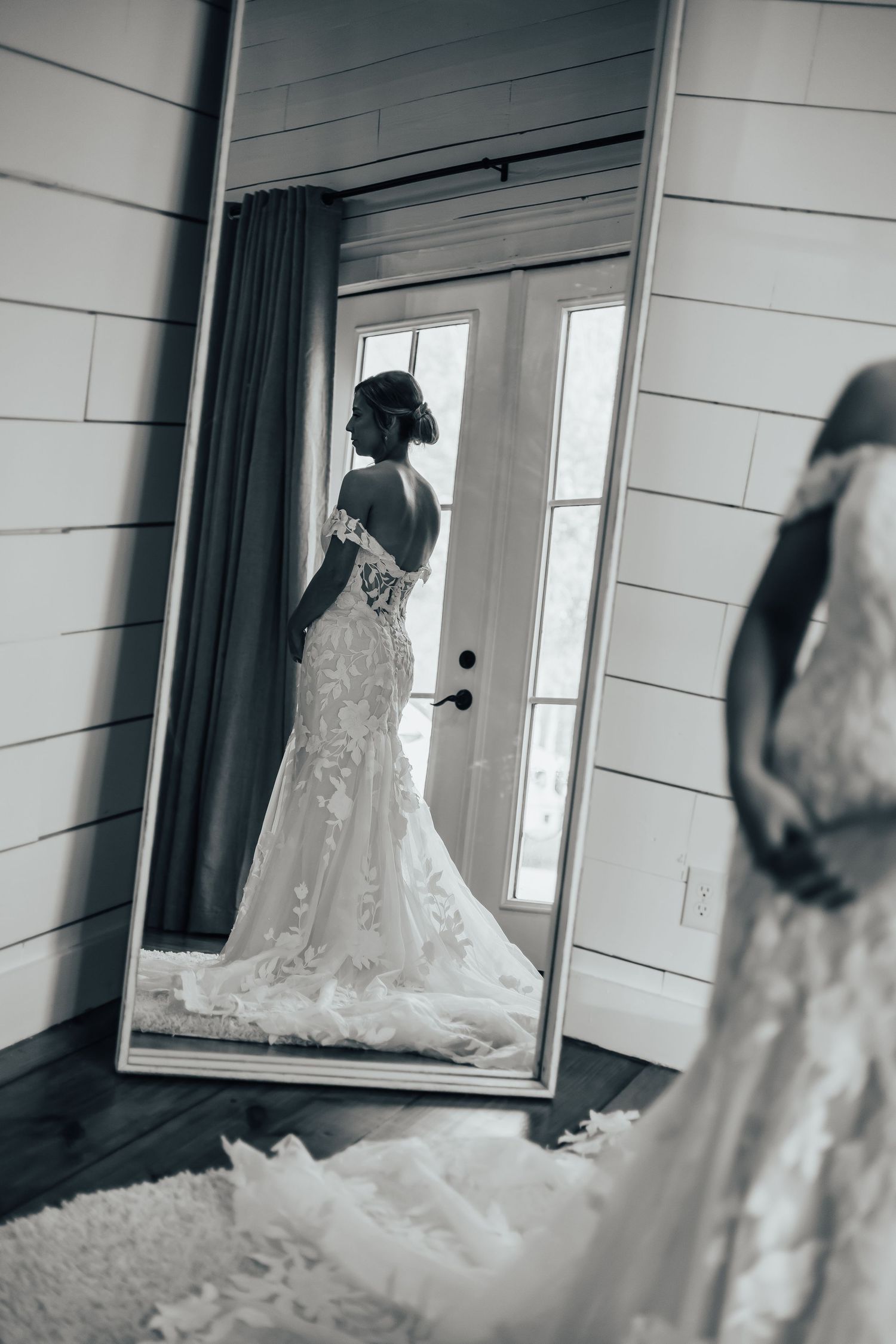 Black and white photo of a bride in a lace mermaid gown reflected in a full-length mirror.