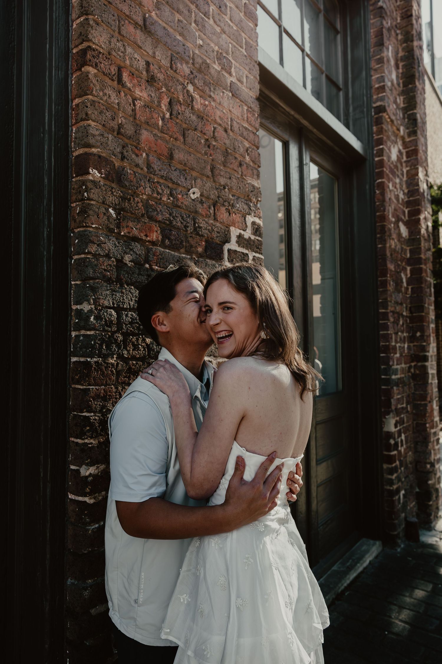 A couple shares intimate moments against a rustic brick wall backdrop in an urban alleyway setting.