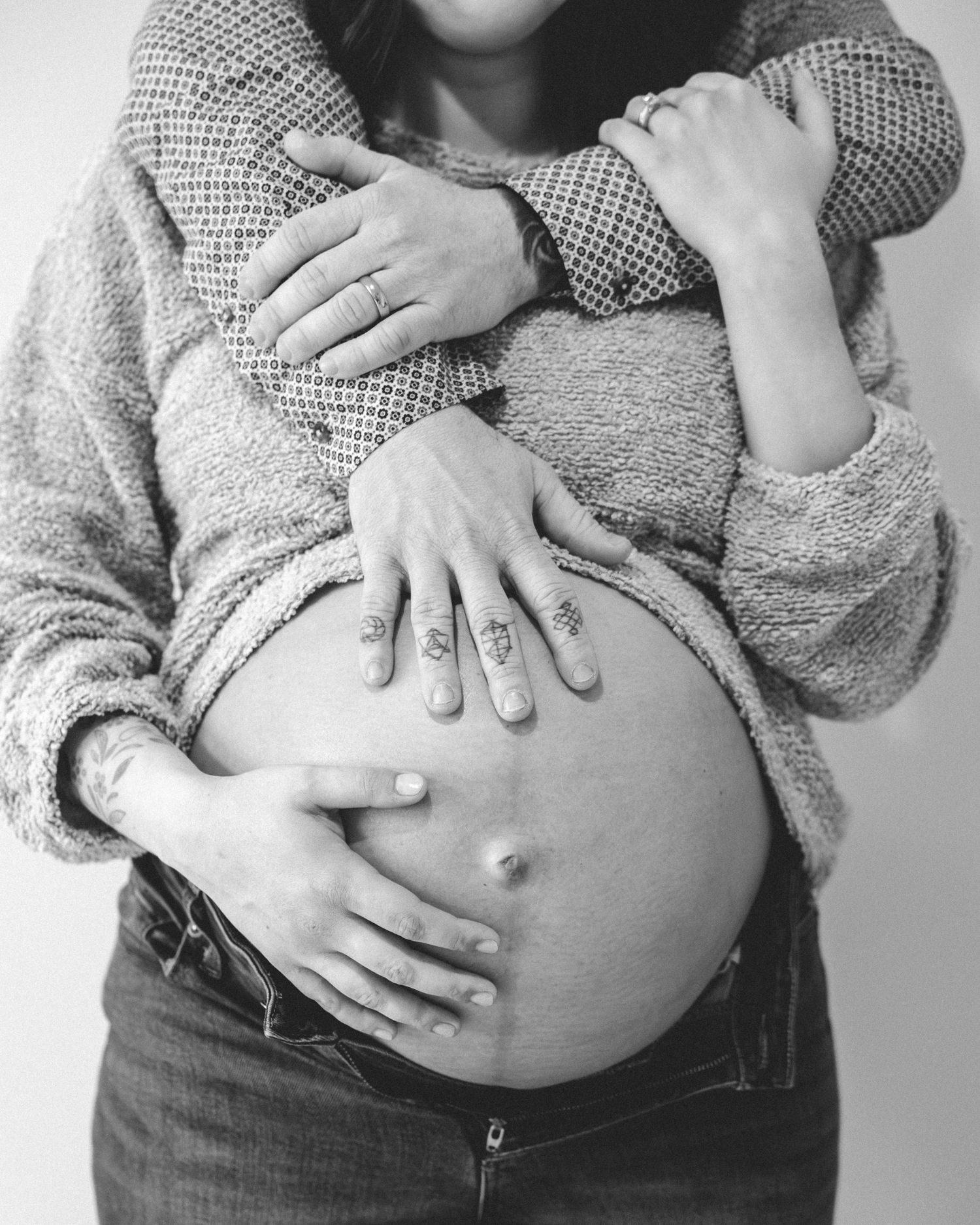 Close up of hands cradling pregnant belly while wearing cozy sweater.