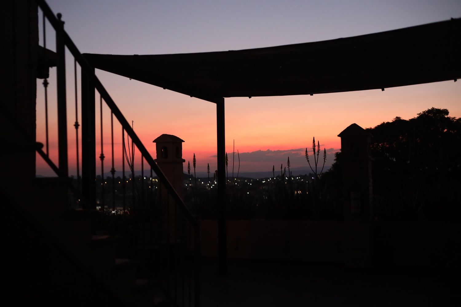 Silhouette of a waterfront terrace at sunset with vibrant orange and pink sky over a marina.