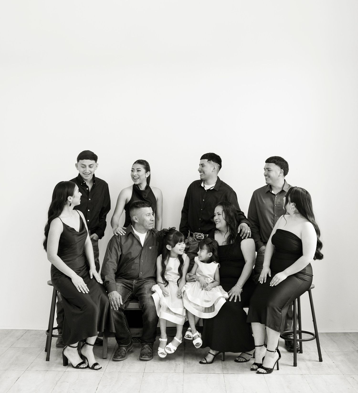 Black and white family portrait of nine people in coordinated dark outfits against a white background.